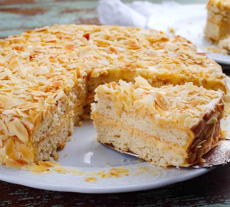 Die Torte auf einem rustikalen Holztisch mit Mandelblättchen drum herum. Alles direkt von vorne fotografiert. | © Shutterstock/ hlphoto