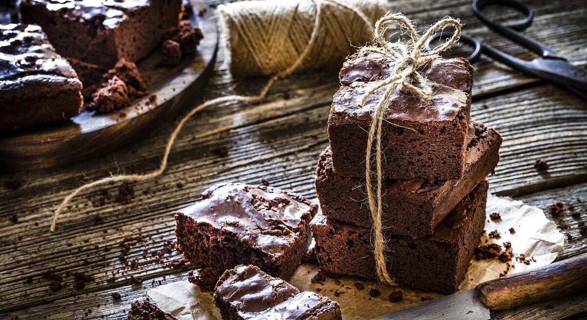 Klassische Brownies, mal einzeln, mal gestapelt / Untergrund grobes Holz /  Messer aus Metall / Kuchengitter / 