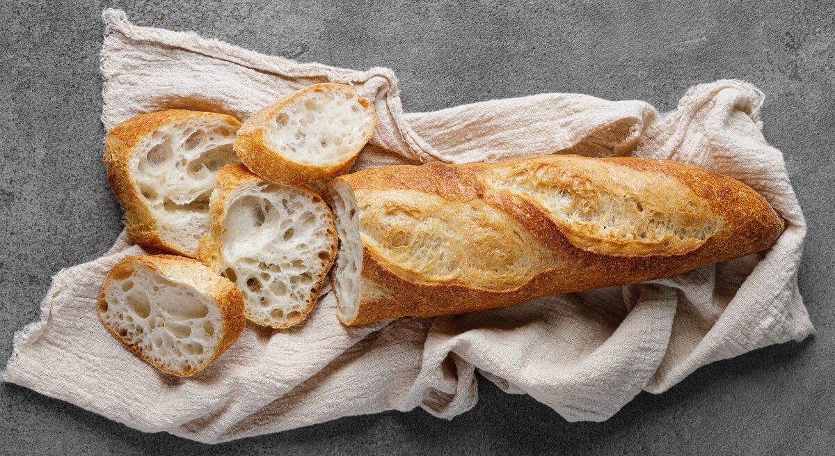 Das Baguette auf einem grauen Tisch mit beiger Tischdecke. Alles von oben fotografiert.