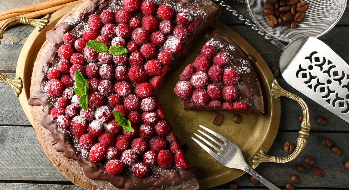 Himbeer-Schokokuchen mit Puderzucker bestreut auf rustikalem Holztisch, neben Kaffeebohnen.