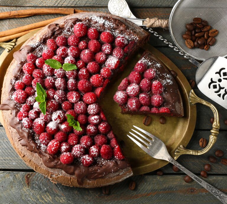 Himbeer-Schokokuchen mit Puderzucker bestreut auf rustikalem Holztisch, neben Kaffeebohnen. | © Shutterstock/ Africa Studio