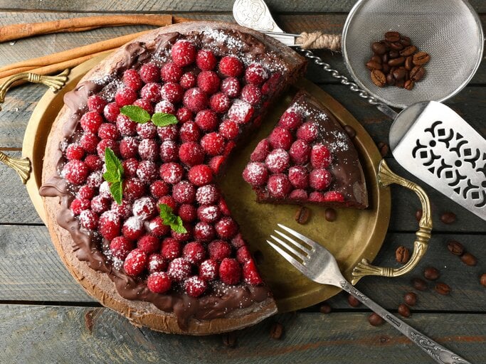 Himbeer-Schokokuchen mit Puderzucker bestreut auf rustikalem Holztisch, neben Kaffeebohnen. | © Shutterstock/ Africa Studio