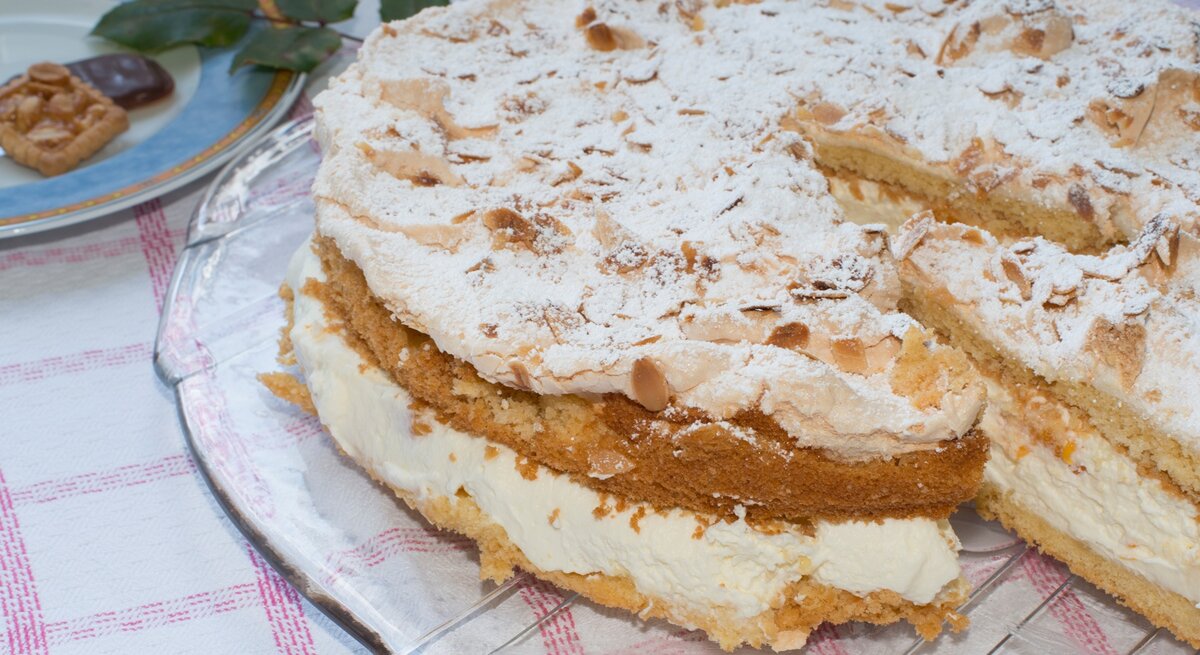 Die Sahnetorte mit Baiserschicht und mandeln auf einem Tisch mit rot-weiß-karierter Tischdecke