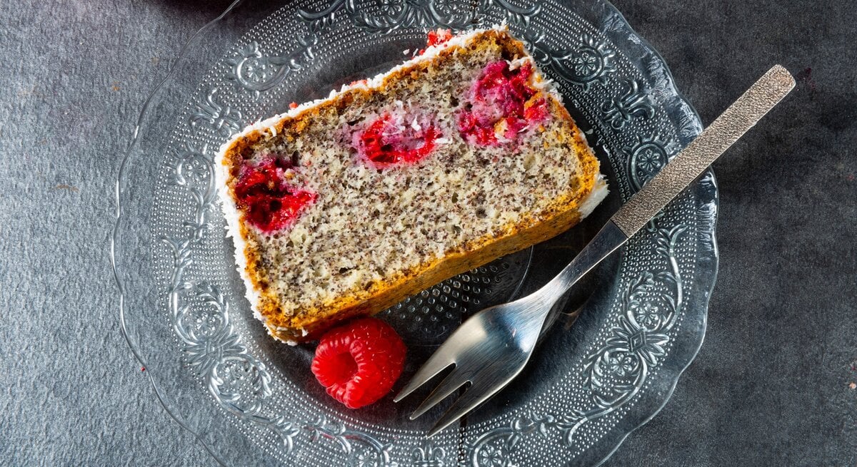Mohnkuchen mit Himbeeren / eine Scheibe vom kastenkuchen / runder Teller aus Glas / eine frische Himbeere / Kuchengabel / Draufsicht