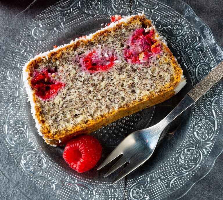 Mohnkuchen mit Himbeeren / eine Scheibe vom kastenkuchen / runder Teller aus Glas / eine frische Himbeere / Kuchengabel / Draufsicht | © Adobe Stock / Darius Dzinnik