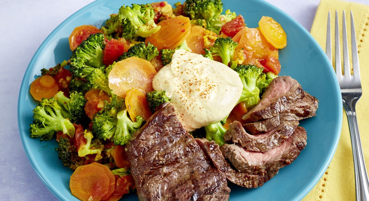 Hüftsteak mit Brokkoli-Möhren-Mix und griechischem Joghurt auf rundem Teller / Draufsicht, schräg