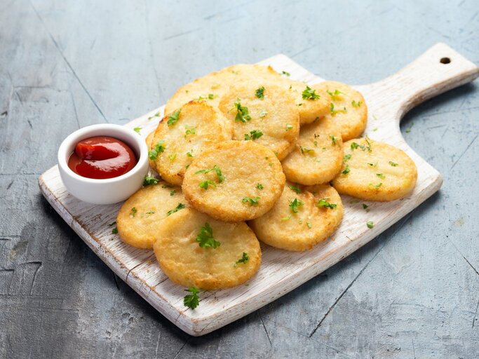 Mehrere flache Blumenkohlpuffer auf einem Holzbrett, daneben Ketchup.  | © GettyImages/DronG