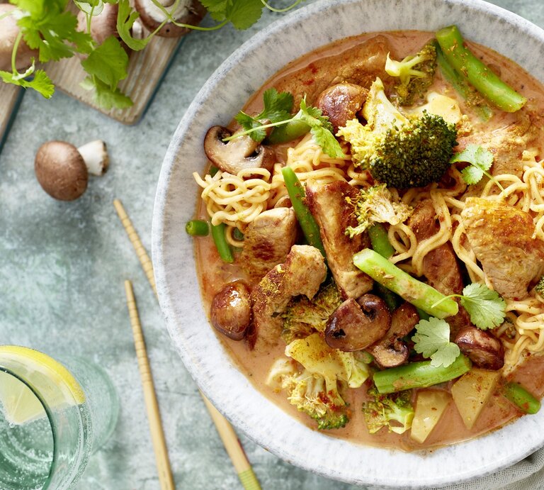 Ein helle Teller mit dem Thai-Curry auf einem hellblauem Untergrund mit grünem Gemüse und Pilzen daneben. Alles direkt von oben fotografiert. | © EAT CLUB/ Isabell Triemer