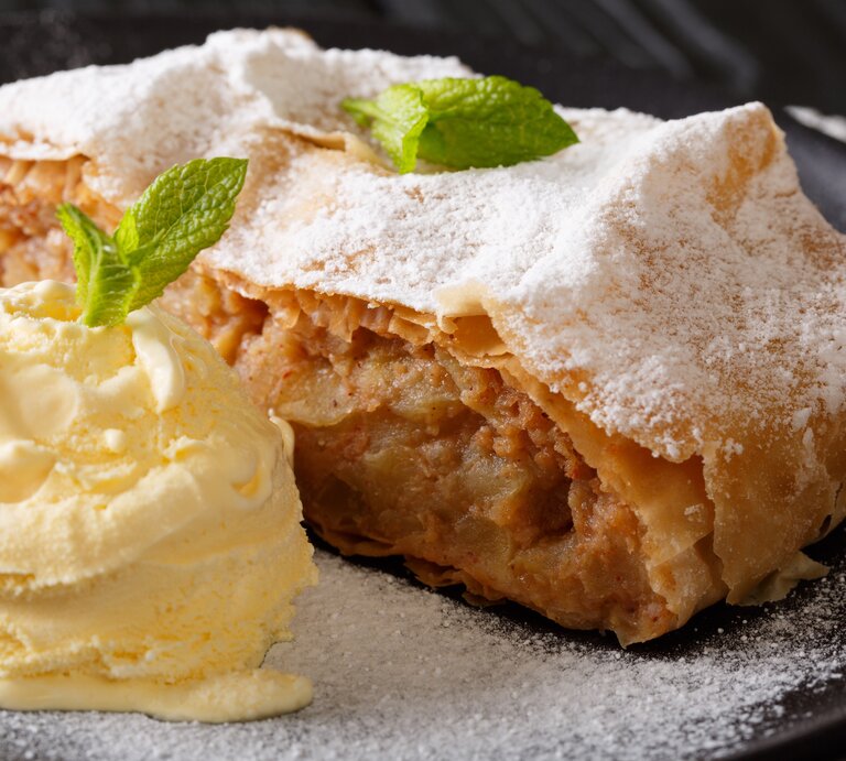 Stück Apfelstrudel auf Teller, daneben Vanilleeis. | © AdobeStock/FomaA