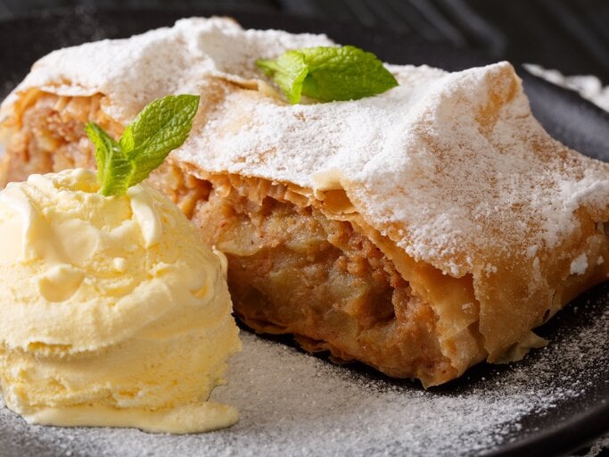 Stück Apfelstrudel auf Teller, daneben Vanilleeis. | © AdobeStock/FomaA