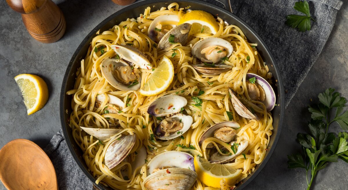 Ein schwarzer Teller mit einer Portion Spaghetti Vongole auf einem grauen Tisch von oben fotografiert