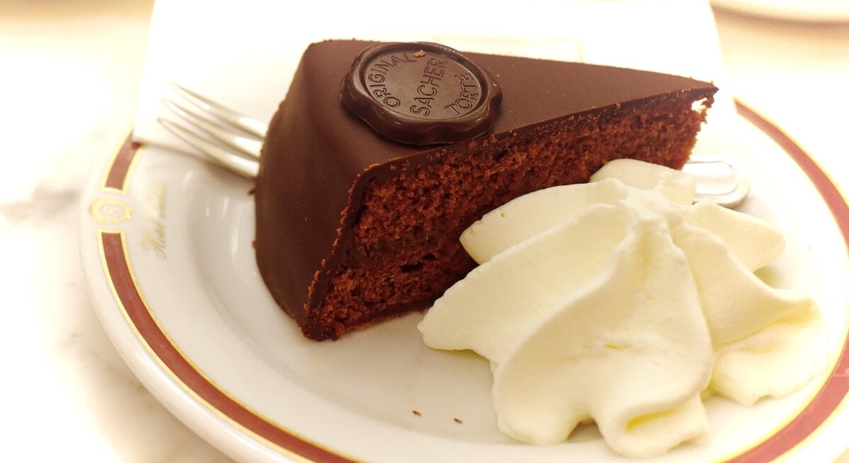 Ein Stück Sachertorte / aufgeschlagene Sahne / Kuchengabel / runder Kuchenteller / Draufsicht schräg