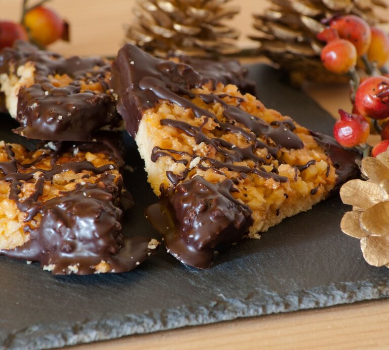 Klassische Nussecken mit Mürbeteig, karamellisierter Nuss-Schicht und Schokoladendekor, arrangiert auf einer Schieferplatte mit weihnachtlicher Dekoration. | © AdobeStock/frittipix
