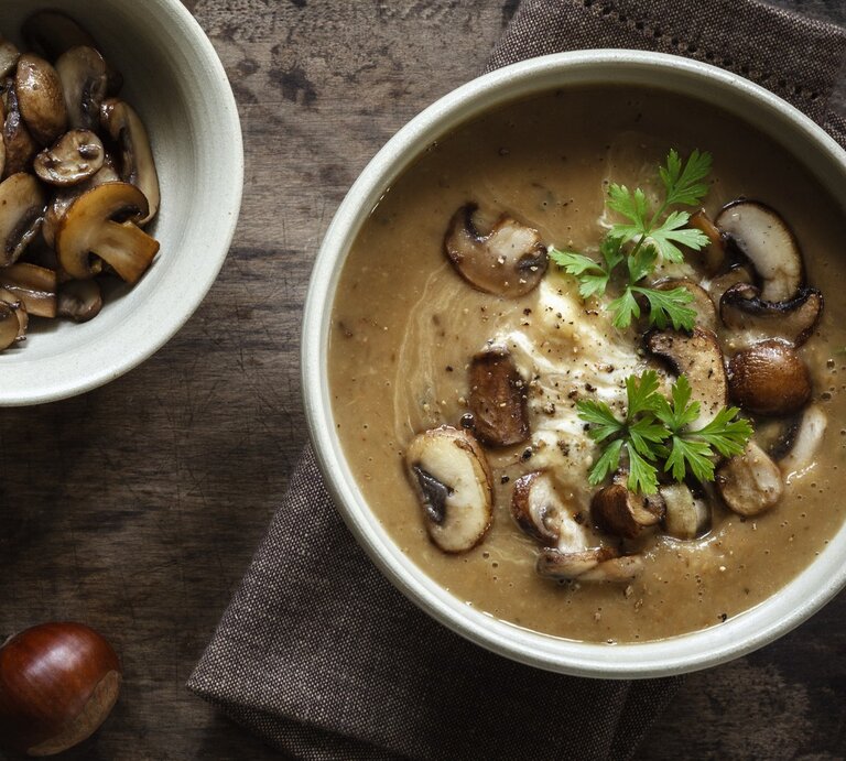 Dunkler Untergrund mit einer Schüssel der Suppe sowie frischen Champignons und Esskastanien drum herum. Alles direkt von oben fotografiert. | © GettyImages/ Westend61