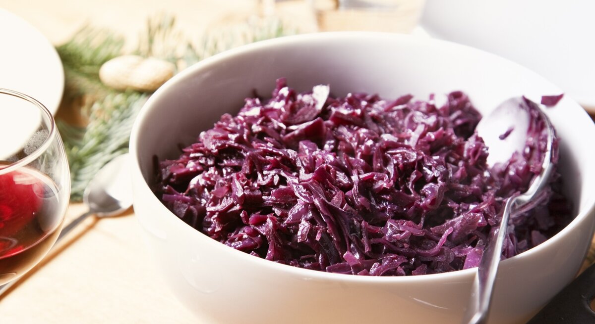 Eine weiße Schale mit dem Rotkohl auf einem hellen Holztisch von schräg oben fotografiert.