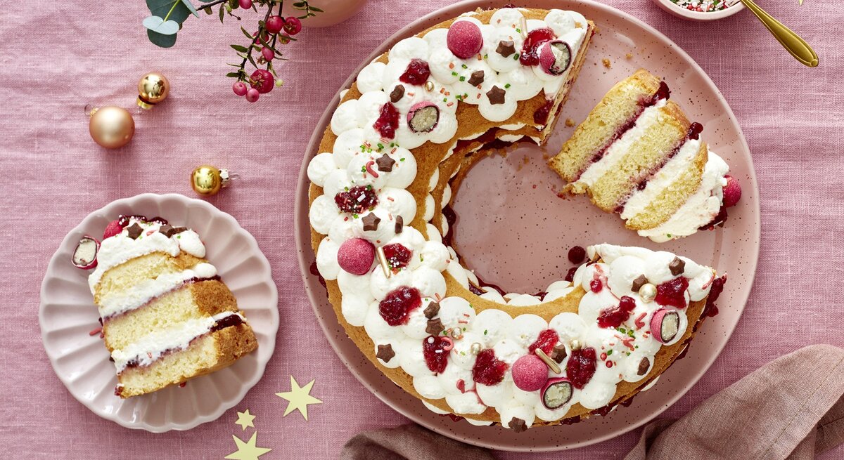 Die angeschnittene Torte auf einer rosa Tischdecke mit viel weihnachtlicher Dekoration. Alles direkt von oben fotografiert.