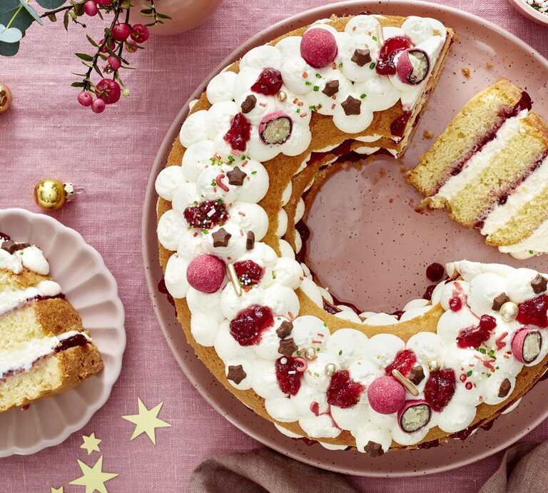 Die angeschnittene Torte auf einer rosa Tischdecke mit viel weihnachtlicher Dekoration. Alles direkt von oben fotografiert. | © EAT CLUB/ Isabell Triemer