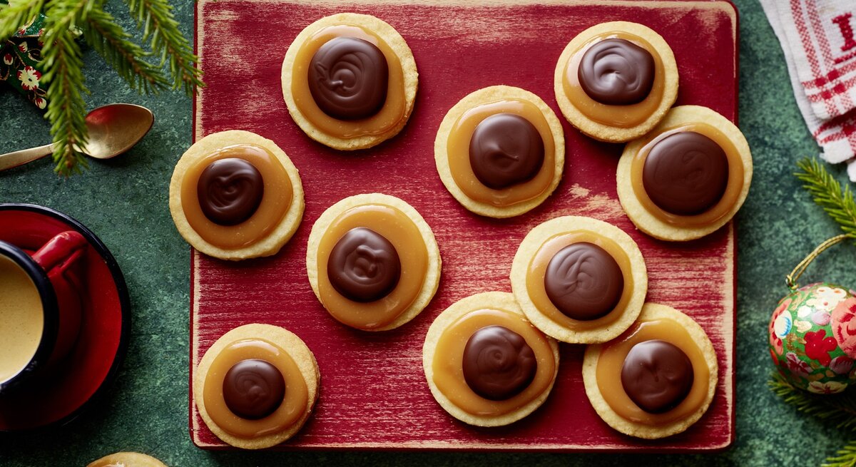 Die Toffifee-Taler auf einem rötlichen Schneidebrett und weihnachtlicher Deko drumherum. Alles direkt von oben fotografiert.