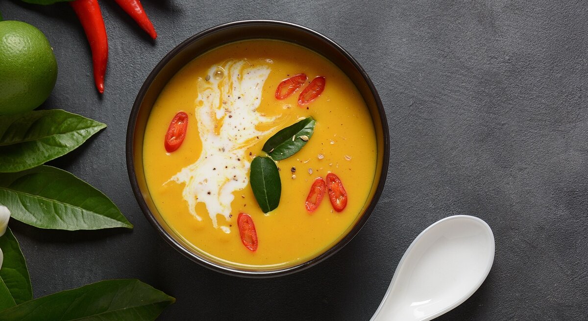 Eine dunkle Schale mit der orangen Suppe auf einem grauen Tisch direkt von oben fotografiert