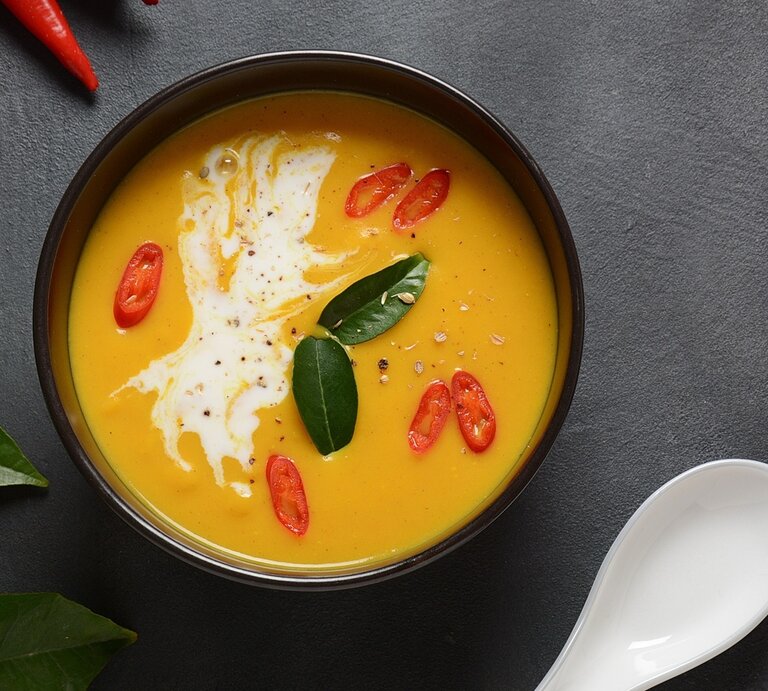 Eine dunkle Schale mit der orangen Suppe auf einem grauen Tisch direkt von oben fotografiert | © Shutterstock/ Natalia Hanin