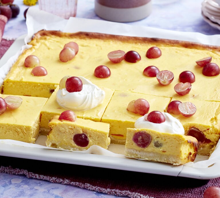 Ein weißes Blech mit dem Kürbis-Trauben-Cheesecake auf einem blau-weißem Marmortisch von schräg oben fotografiert | © EAT CLUB/ Isabell Triemer