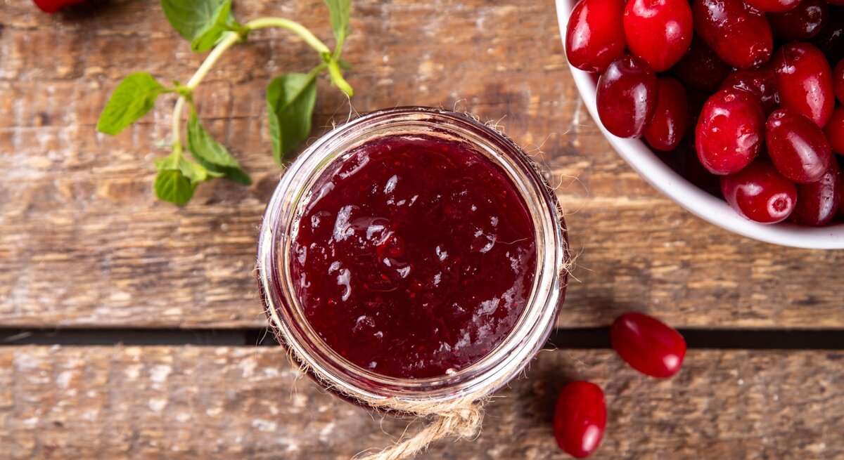 Draufsicht: Eine selbst gemachte Kornelkirschen-Marmelade / Drumherum frische Kornelkirschen / Untergrund Holz /