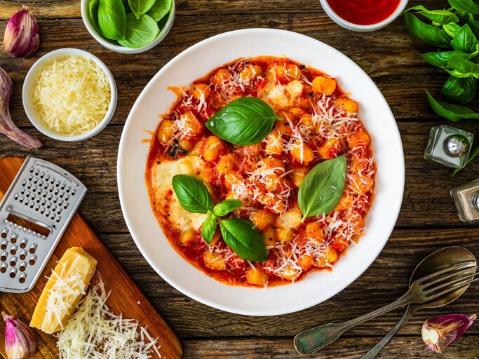 Frisch zubereitete Gnocchi in Tomatensauce mit Basilikumblättern und geriebenem Parmesan auf rustikalem Holztisch. | © AdobeStock/Jacek Chabraszewski