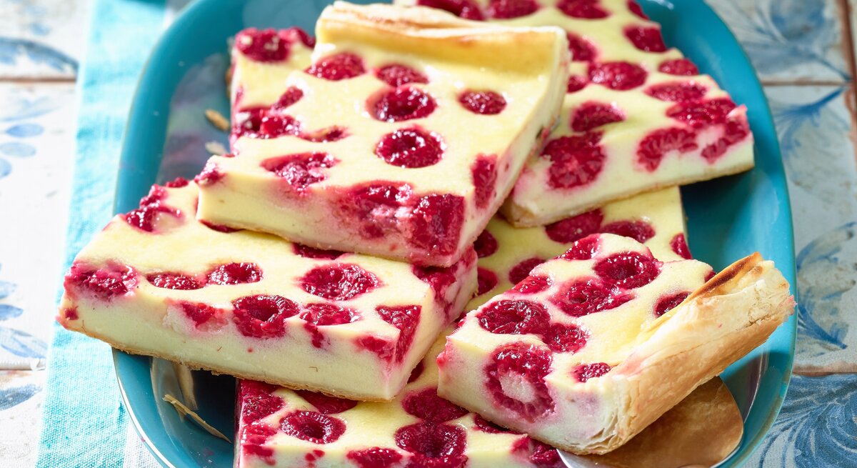 Türkisfarbener Teller mit Stücken von Himbeer-Käsekuchen, appetitlich angerichtet auf rustikalem Untergrund.