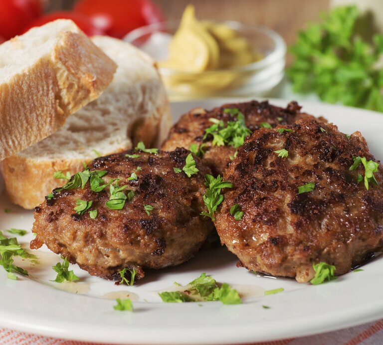 Mehrere Frikadellen bestreut mit Kräutern auf weißem Teller neben Brotscheiben.  | © AdobeStock/der hugo2