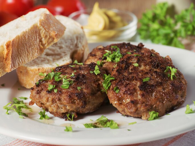 Mehrere Frikadellen bestreut mit Kräutern auf weißem Teller neben Brotscheiben.  | © AdobeStock/der hugo2