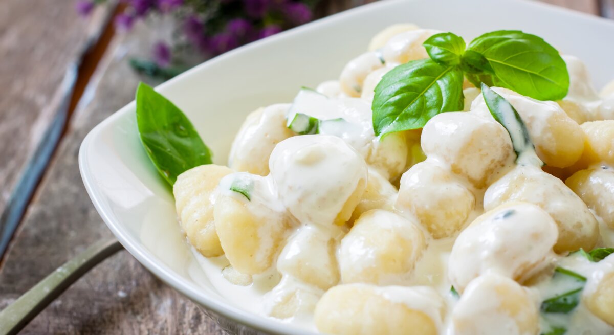 Ein weißer Teller befüllt mit Low-Carb-Gnocchi in cremiger Soße auf Holztisch.