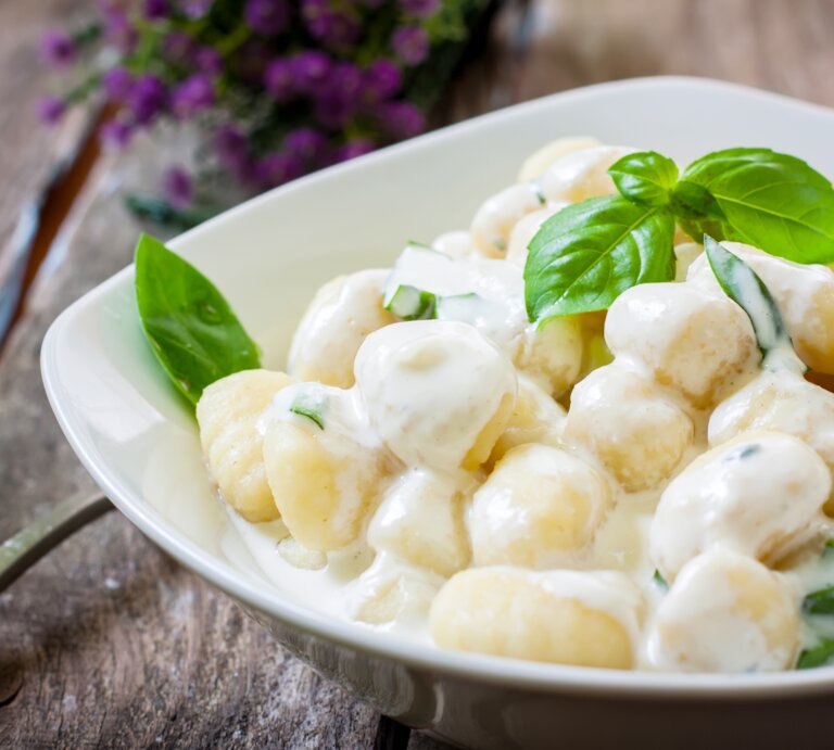 Ein weißer Teller befüllt mit Low-Carb-Gnocchi in cremiger Soße auf Holztisch. | © AdobeStock/Ramon Grosso