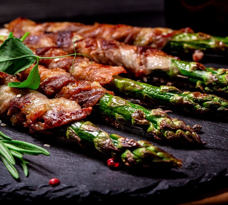 Appetitlicher Blick auf gebratenen Spargel in Speckmantel, fein gewürzt mit Kräutern auf Steinplatte. | © Shutterstock/sweet marshmallow
