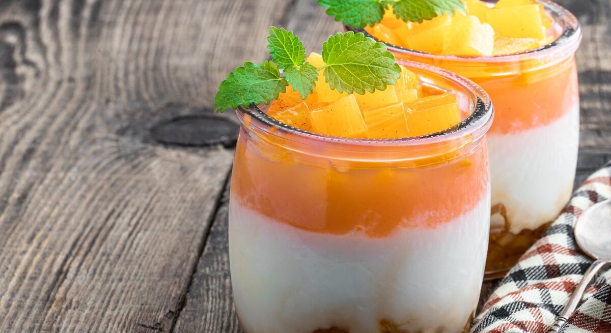 Solero-Dessert im Glas, mit frischen Pfirsichstücken und Minze dekoriert, auf einem rustikalen Holztisch angerichtet.