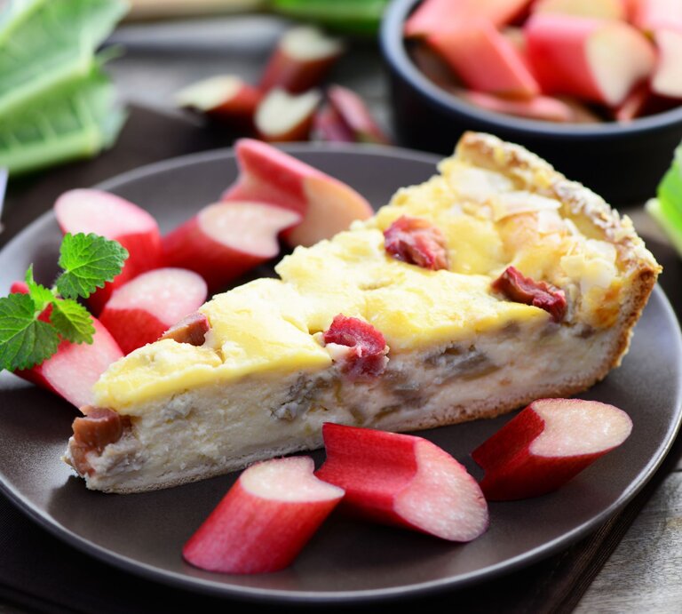 Cremiger Rhabarberkuchen mit frischen Stücken auf dunklem Teller, garniert mit Minzblättern. | © Shutterstock/photocrew1