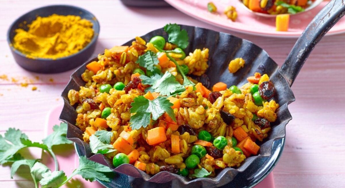 Appetitliche Schüssel mit orientalisch gebratenen Haferflocken, die mit verschiedenen Gemüsen wie Karotten und Erbsen sowie Gewürzen zubereitet wurden. Das Gericht wird mit frischen Kräutern garniert.
