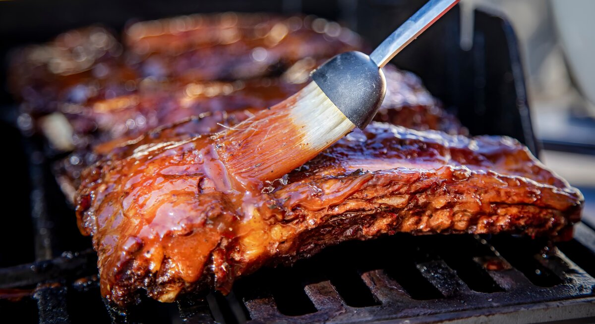 Die Spareribs von der Seite auf dem Grill fotografiert, während sie gerade mit Marinad eeingepinselt werden.