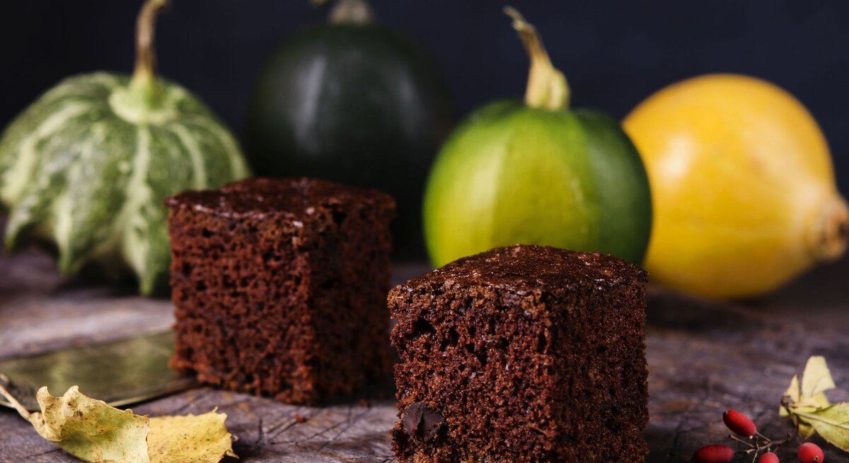 Im Hintergrund sind Zucchinis aus dem Garten zu sehen, vorne zwei schmackhafte Browsnies aus Schokolade und Zucchini.