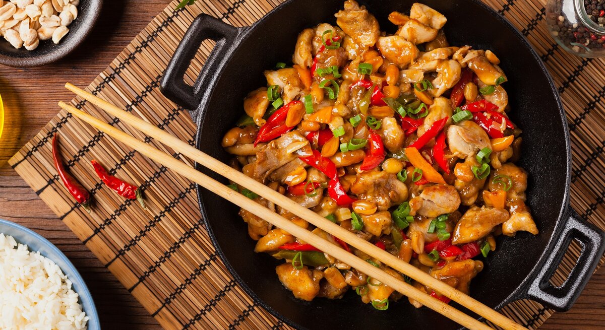 Ein Teller mit dem Wok-Gericht auf einem dunklen Tisch mit asiatischen Deko-Elementen direkt von oben fotografiert.