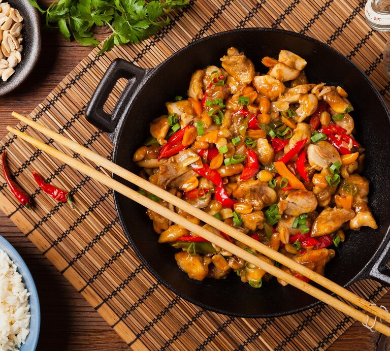 Ein Teller mit dem Wok-Gericht auf einem dunklen Tisch mit asiatischen Deko-Elementen direkt von oben fotografiert. | © Shutterstock/ gkrphoto