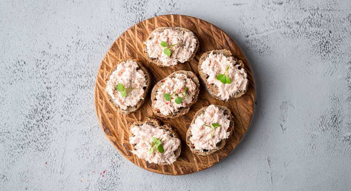 Draufsicht auf  ein Holzbrett, darauf mehrere Scheiben Thunfisch-Bruschetta.