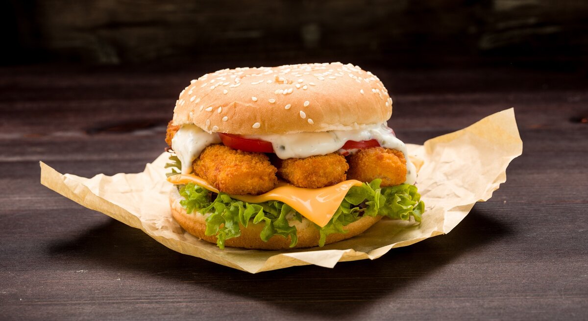 Der Fischstäbchen-Burger auf einem dunklen Tisch und schwarzem Hintergrund. Alles nah und von der Seite fotografiert