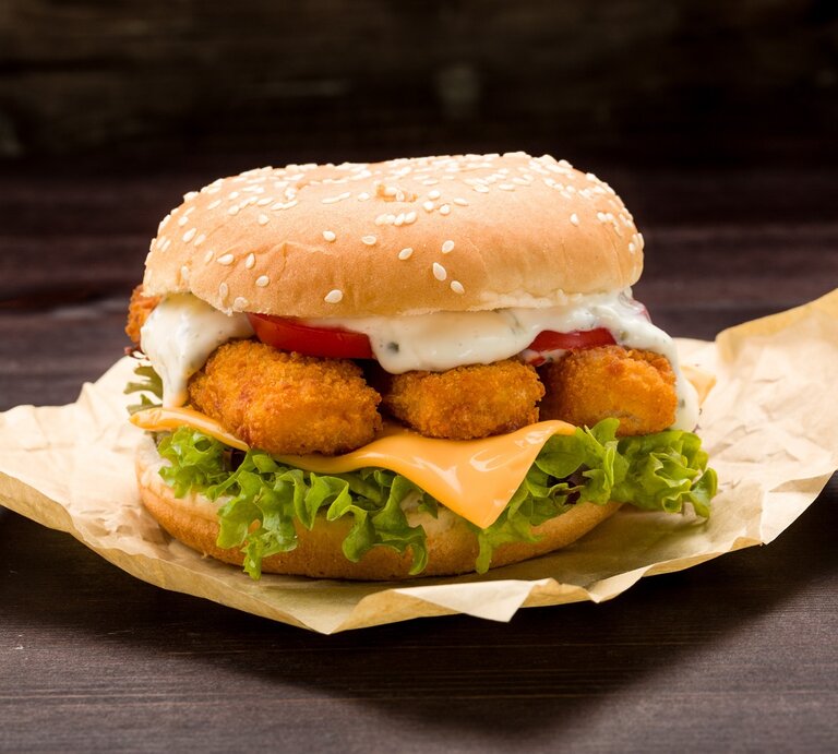 Der Fischstäbchen-Burger auf einem dunklen Tisch und schwarzem Hintergrund. Alles nah und von der Seite fotografiert | © Shutterstock/ Fischer Food Design