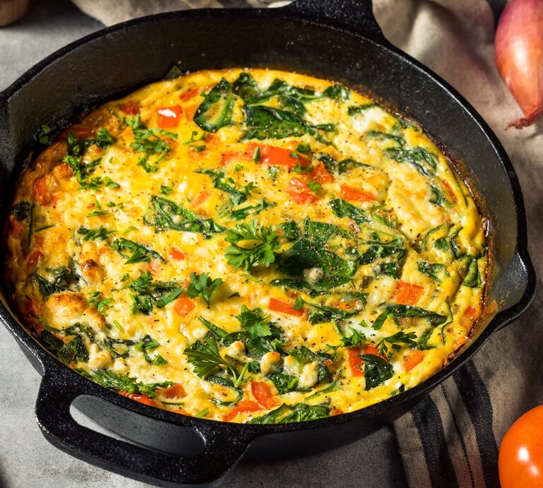 Eine gusseiserne Pfanne mit dem Omelette mit Feta und Tomaten auf einem grauen Steintisch. Alles von schräg oben fotografiert. | © Shutterstock/ Brent Hofacker