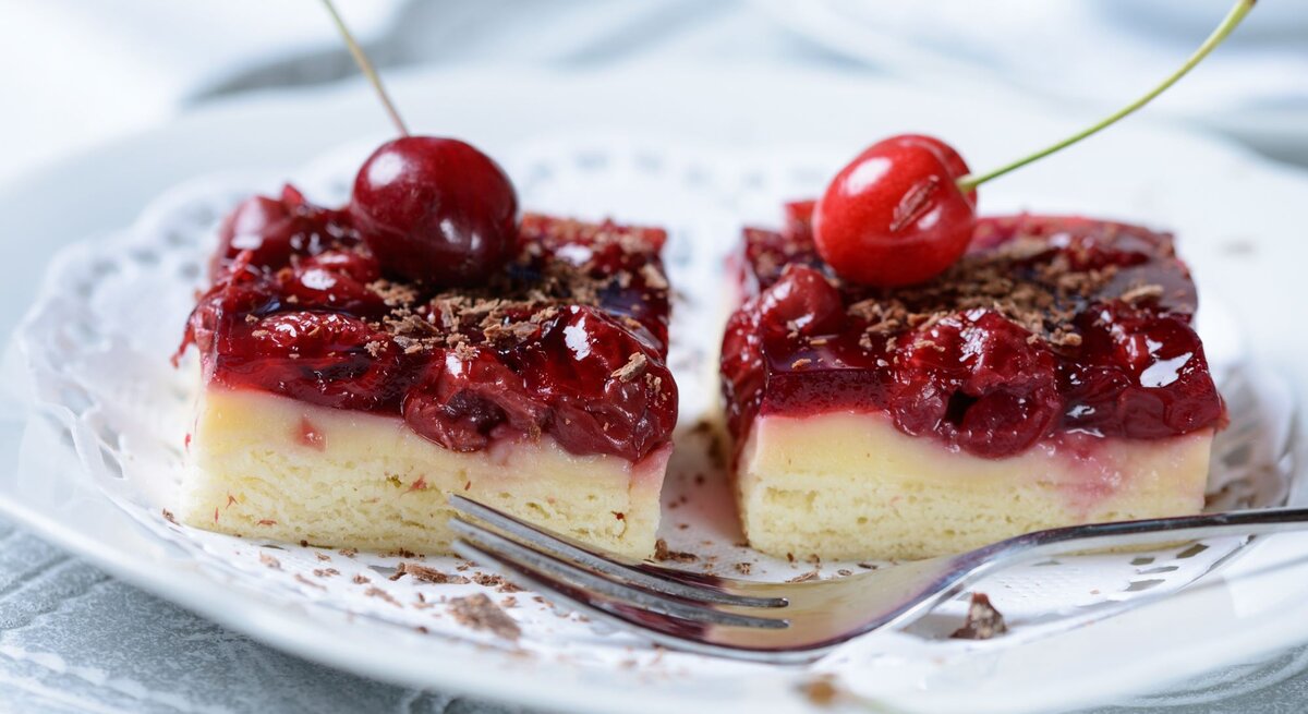 Saftige Kirschtörtchen mit heller Creme und glänzendem Guss, garniert mit frischen Kirschen und geraspelter Schokolade.