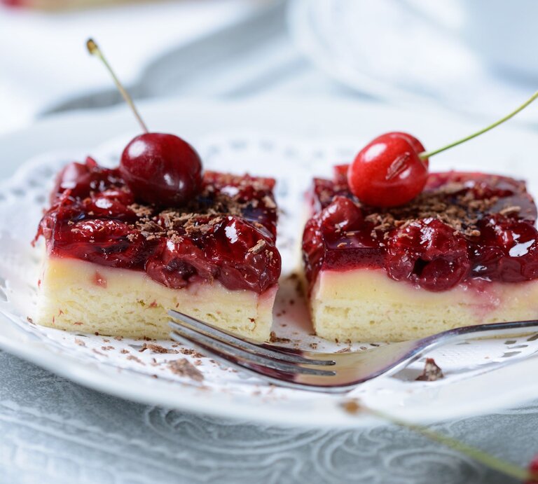 Saftige Kirschtörtchen mit heller Creme und glänzendem Guss, garniert mit frischen Kirschen und geraspelter Schokolade. | © Adobe Stock/ Kitty