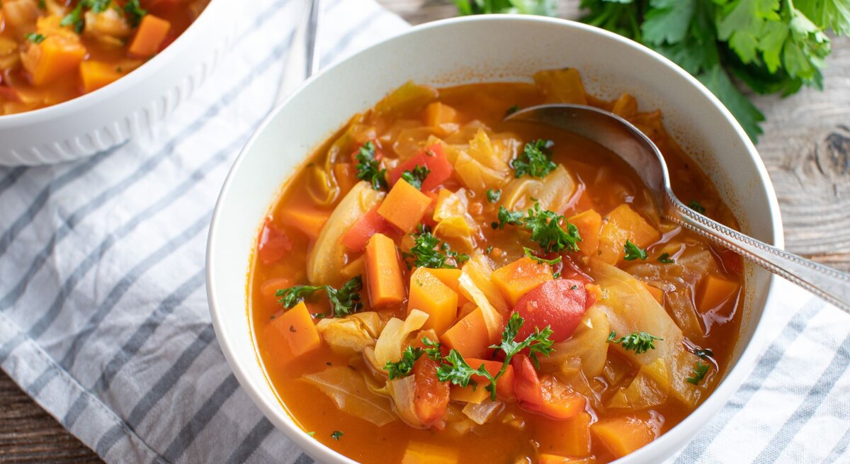 Weiße Schüssel voll Kohlsuppe mit Karotten und Paprika. 