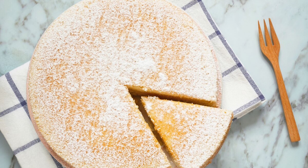Ein Low Carb Joghurtkuchen von oben fotografiert, ein Stück ist angeschnitten und eine Gabel liegt recht davon auf dem Tisch.