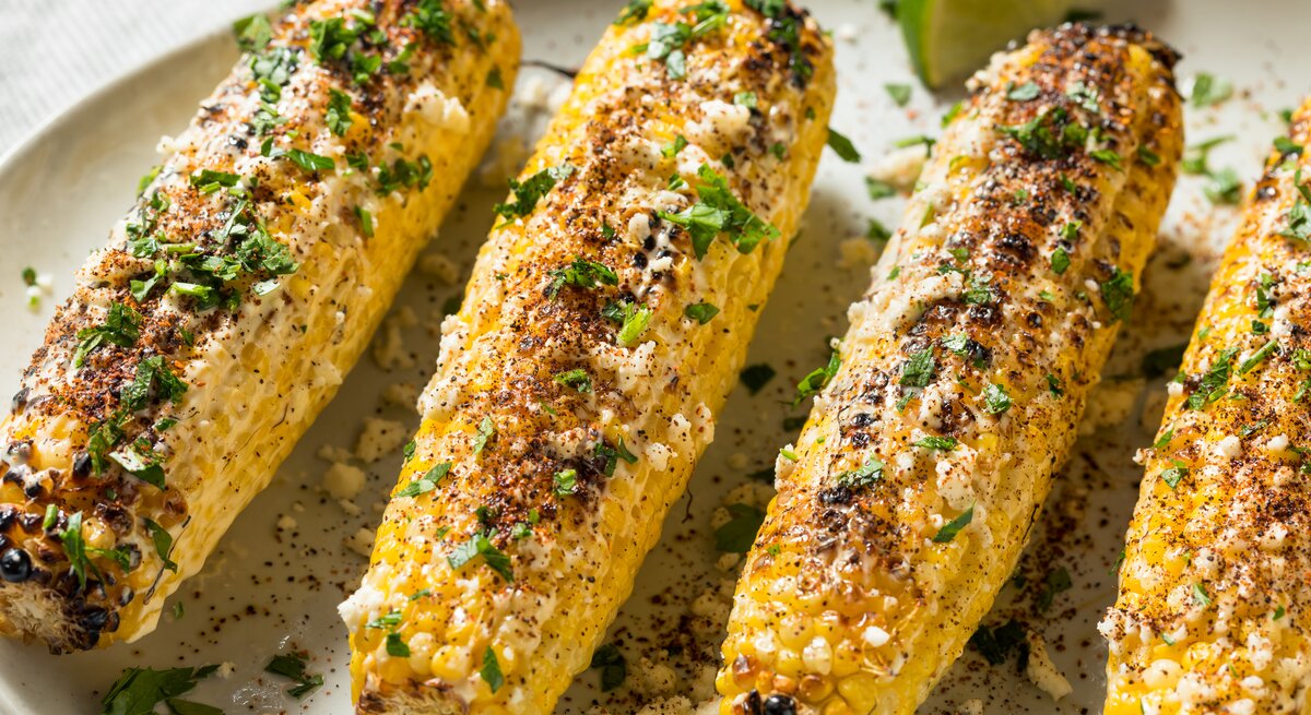 Mehrere Maiskolben bestreut mit Parmesan und Koriander.