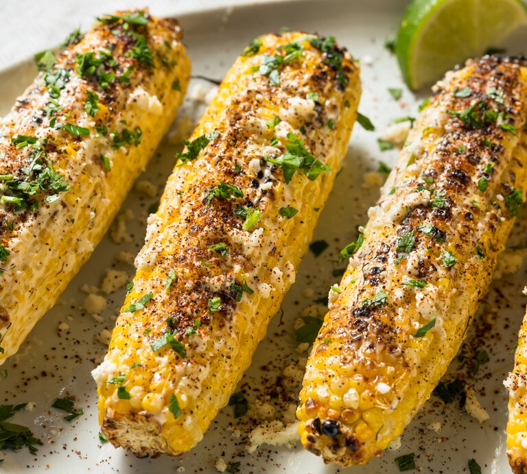 Mehrere Maiskolben bestreut mit Parmesan und Koriander.